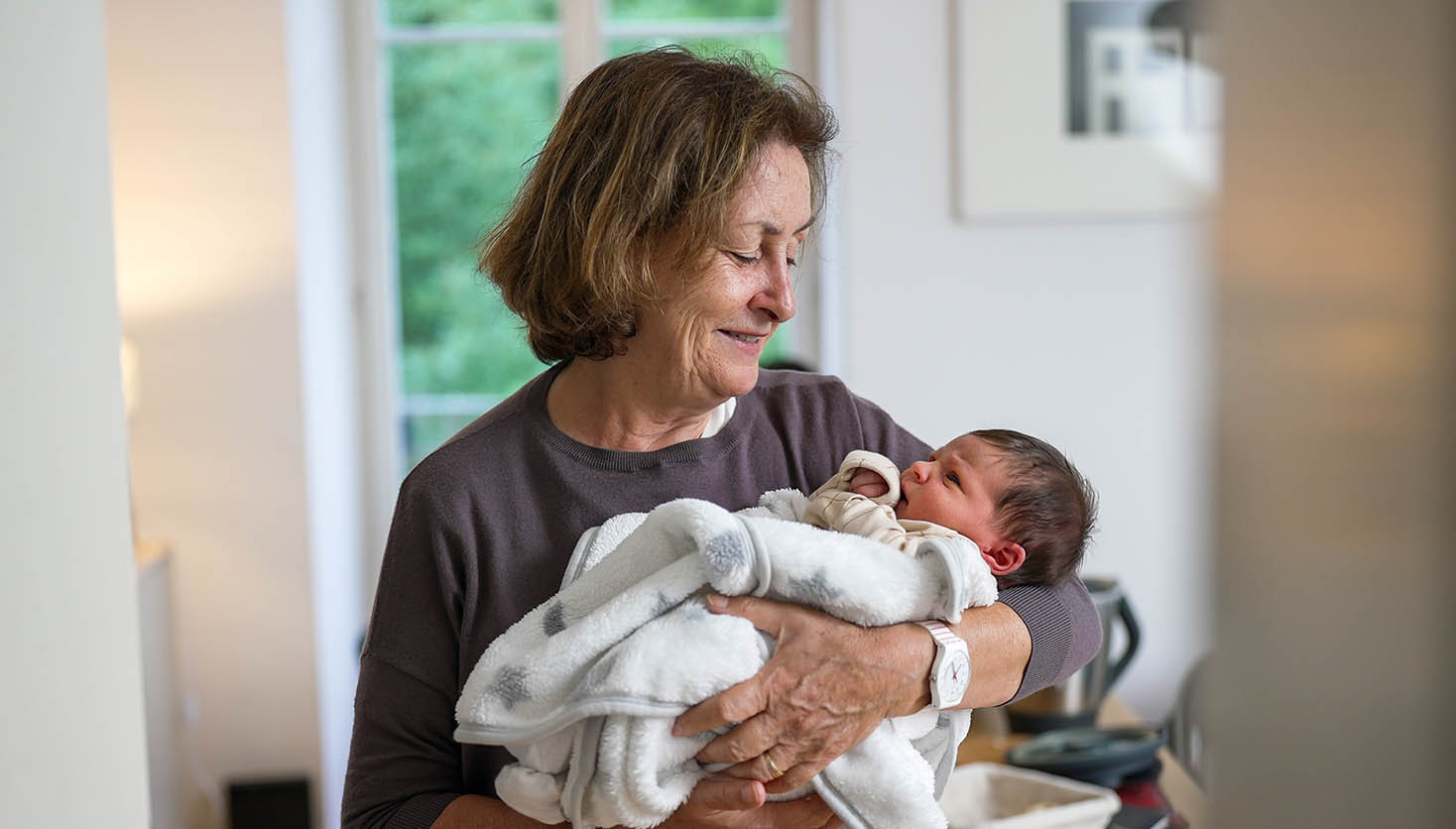 Grandmother,Holding,Newborn,Baby,Wrapped,In,A,White,Blanket,,Looking Grandmother volunteer holding a baby.